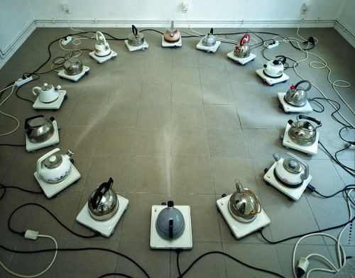 
     <i>Kesseltreiben</i>, 
     1963<br />
     16 kettles, aluminium, stainless steel, sheetiron, 
      Ø 200 cm<br />
     catcalls and flute concerto